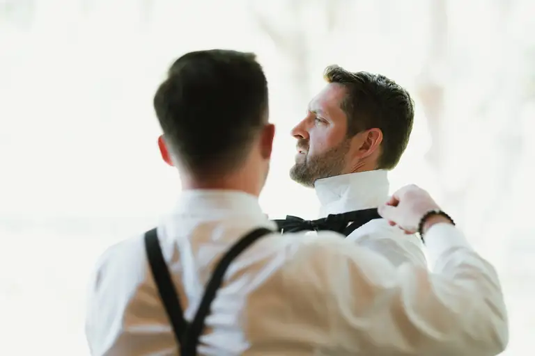 Groom fastening his bow tie while getting ready