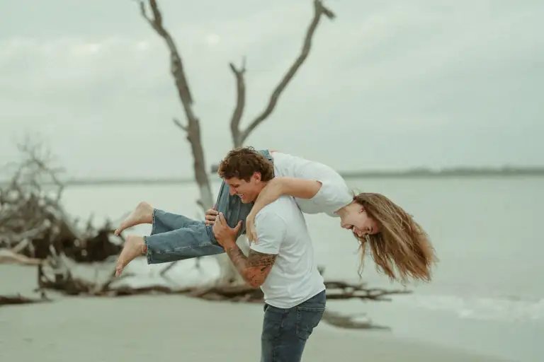 Couple laughing as he lifts her on a driftwood beach