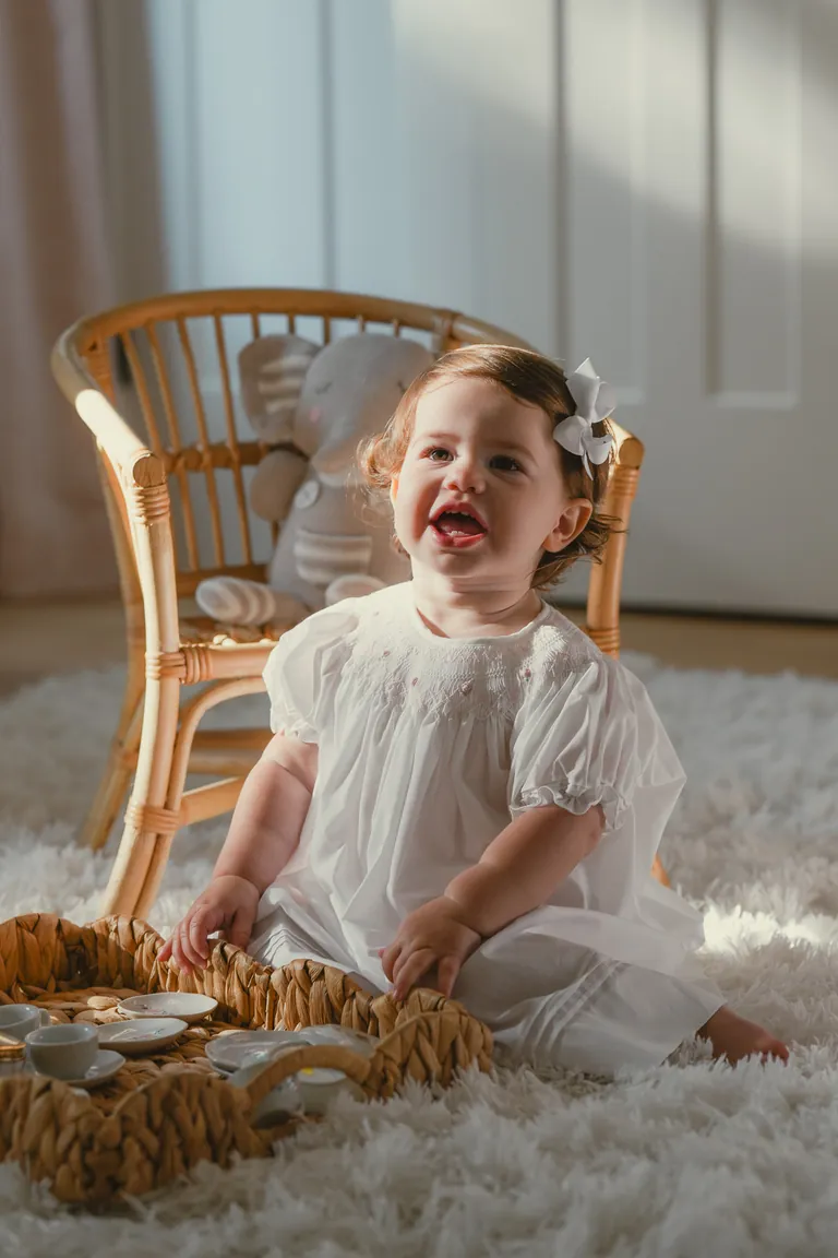 A little girl laughing in a wicker chair on a sheepskin rug