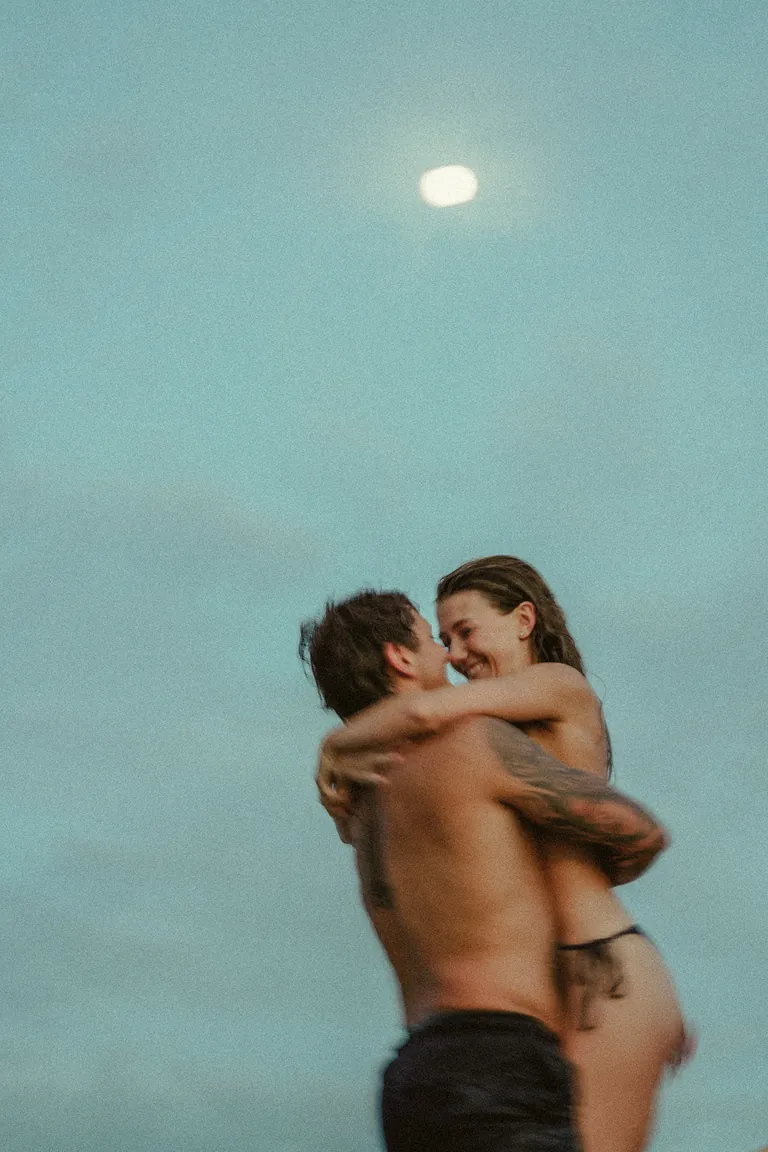 A couple embracing in the sea under a pale full moon