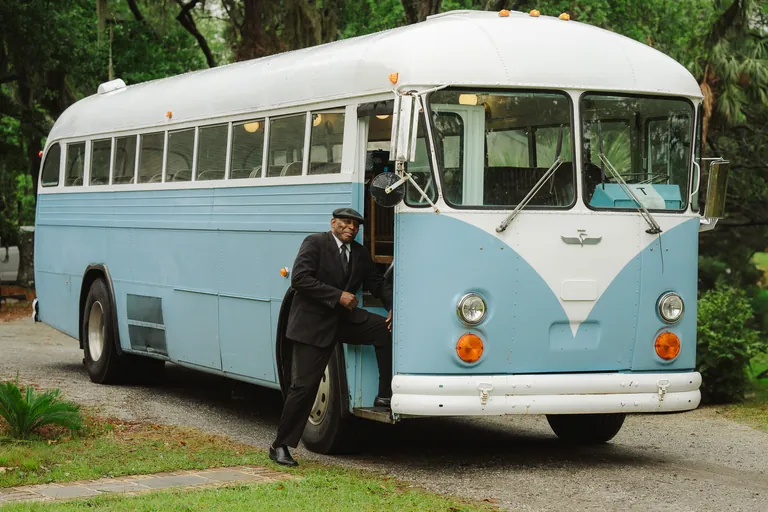A groom stepping off a vintage blue school bus