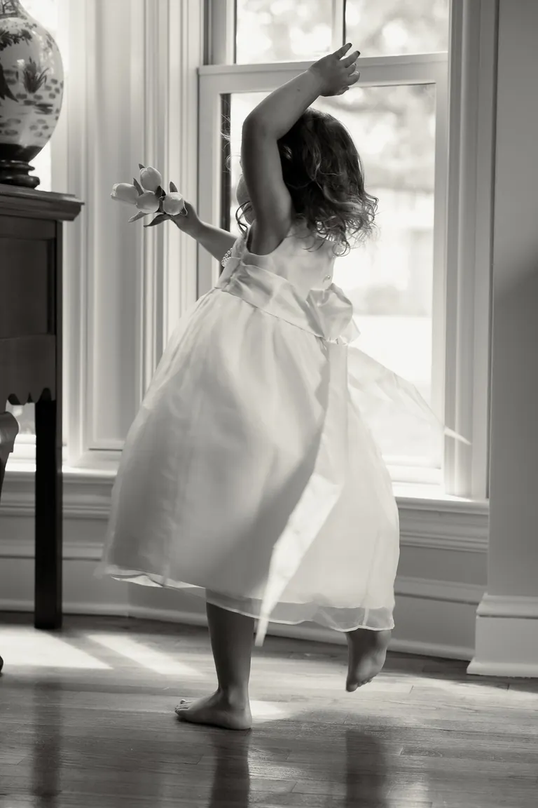 A girl twirling in her party dress in a sunlit doorway, black and white