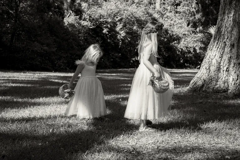 Two flower girls walking through the trees, black and white