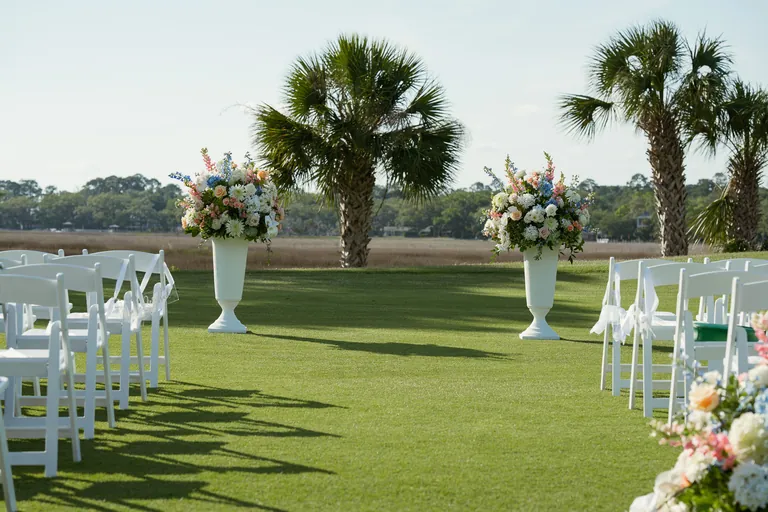 Ceremony chairs and floral arrangements set up on the lawn beneath the palms