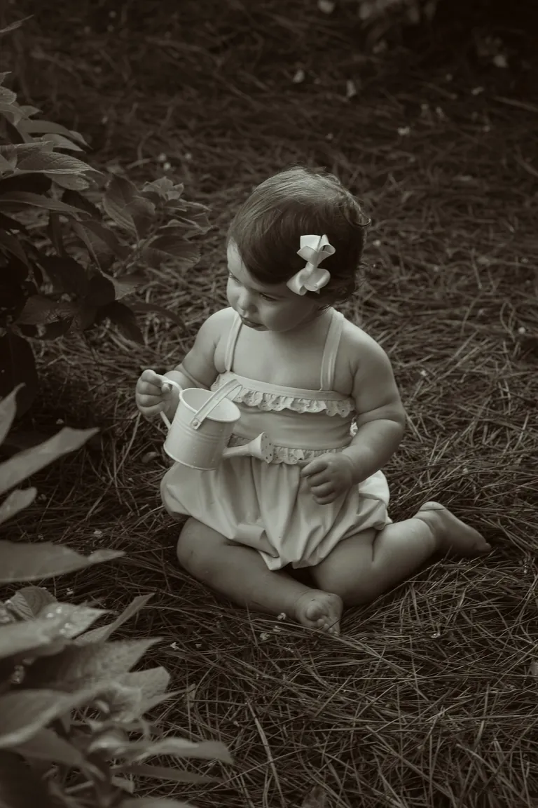 A baby sitting in the dry grass in a bonnet, sepia