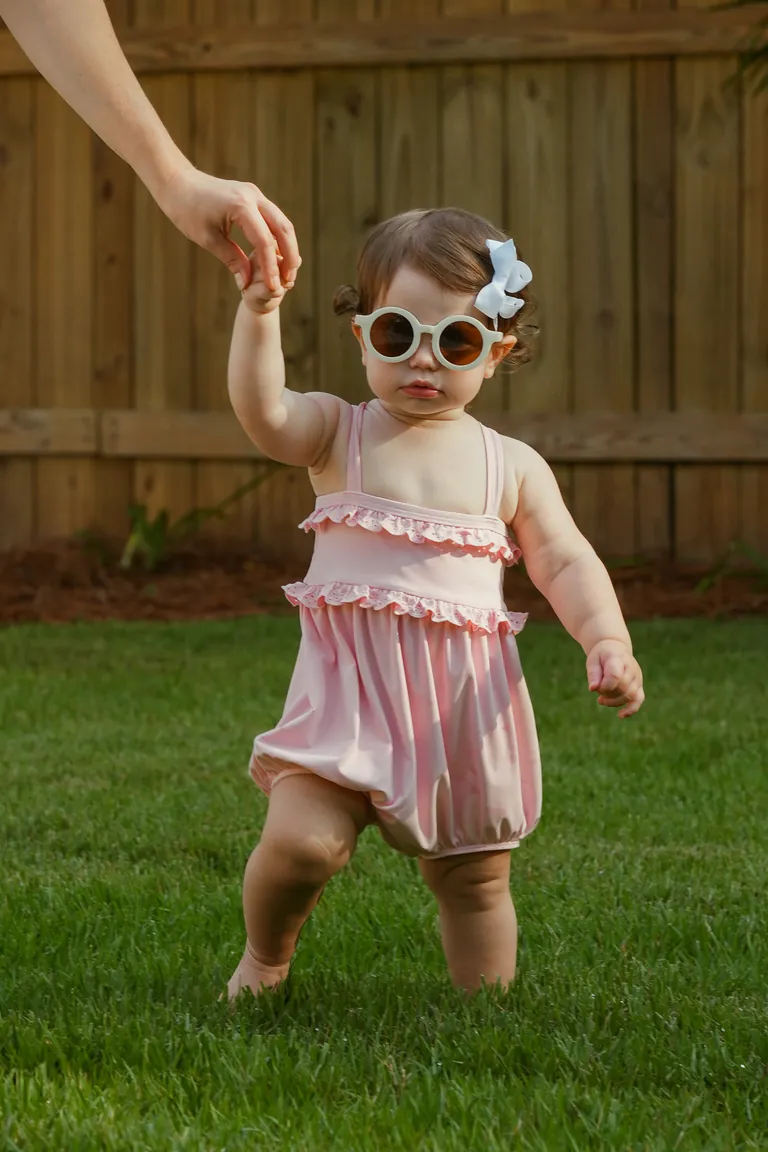A toddler in heart-shaped sunglasses toddling across the grass