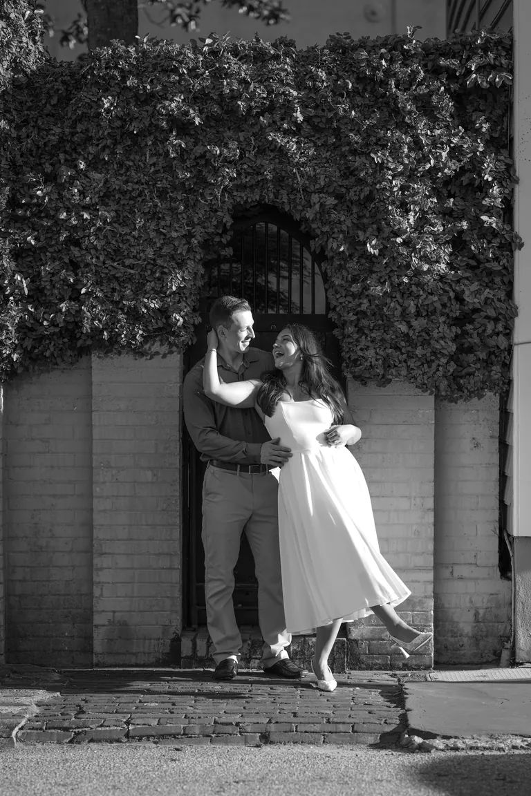A couple kissing beneath an ivy-covered brick arch, black and white